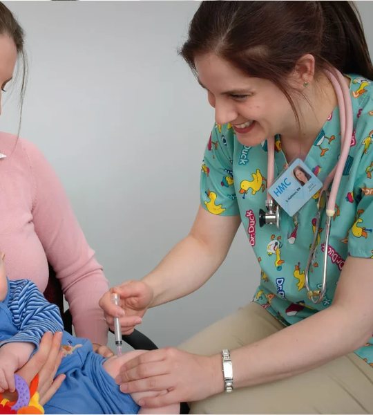 A nurse caring for a baby sitting on his mother's lap